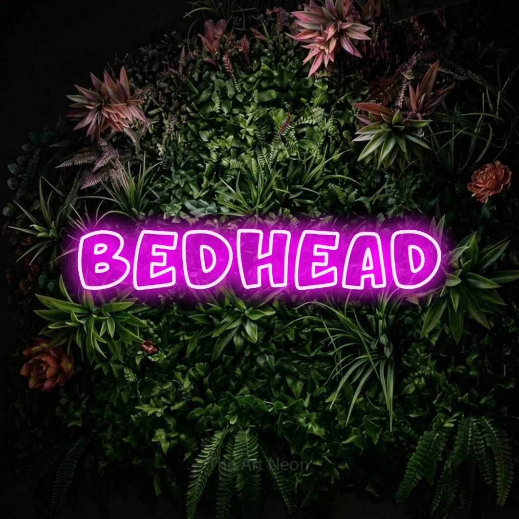 Pink outline-style LED neon sign reading "Bedhead" against a flowering garden wall for bedroom décor