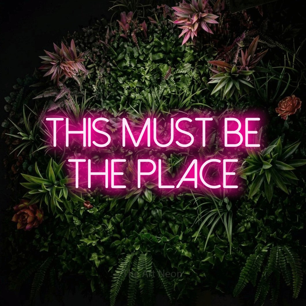 Hot pink LED neon sign reading "This Must Be the Place" against a flowering garden wall for living room décor