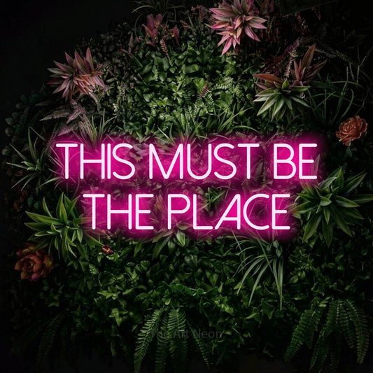 Enseigne néon à DEL à lumière rose vif, affichant « This Must Be the Place » sur un mur de jardin fleuri, pour décorer un salon