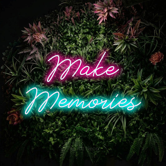 Ice blue and hot pink script-style LED neon sign reading "Make Memories" against a flowering garden wall