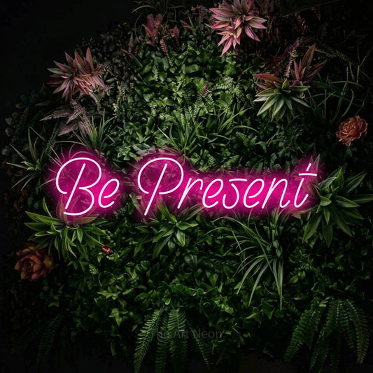 Enseigne néon à DEL à lumière rose vif, affichant « Be Present » sur un mur de jardin fleuri, pour décorer un salon