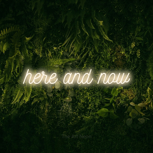 Enseigne néon à DEL à lumière blanche chaude, de style manuscrit, affichant « Here and Now » sur un mur vert couvert de mousse, pour décorer un salon