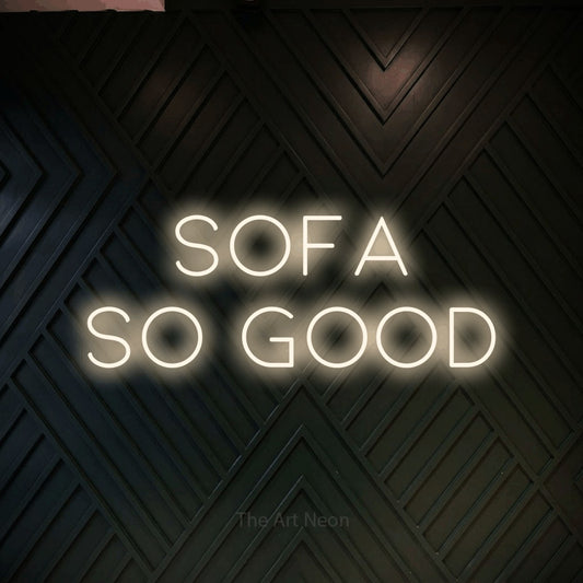 Warm white LED neon sign reading "Sofa So Good" against a dark geometric wood wall for living room décor