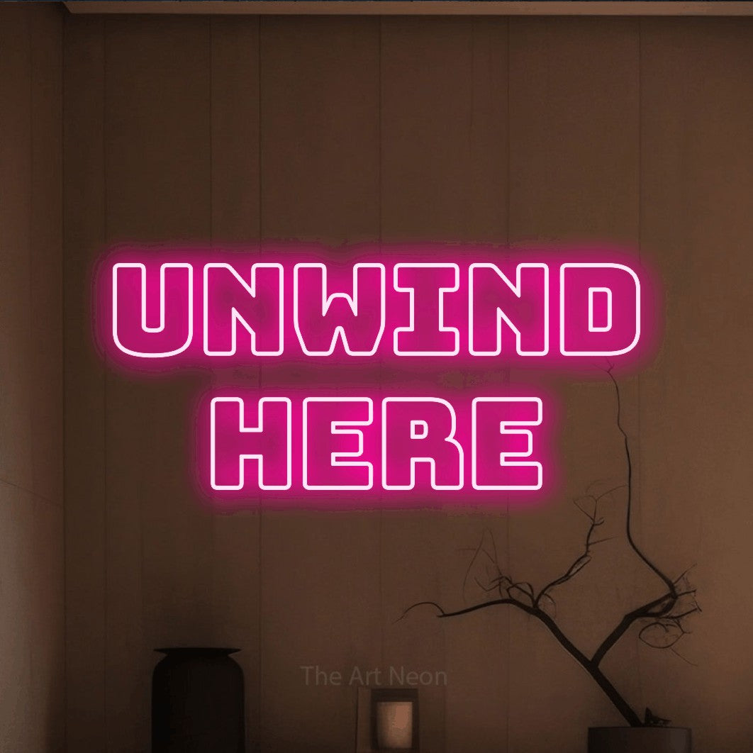 Hot pink outline-style LED neon sign reading "Unwind Here" against a warm brown wall for living room décor
