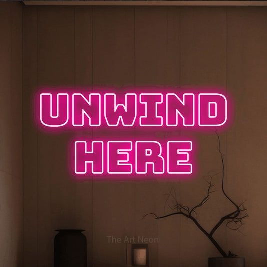 Hot pink outline-style LED neon sign reading "Unwind Here" against a warm brown wall for living room décor