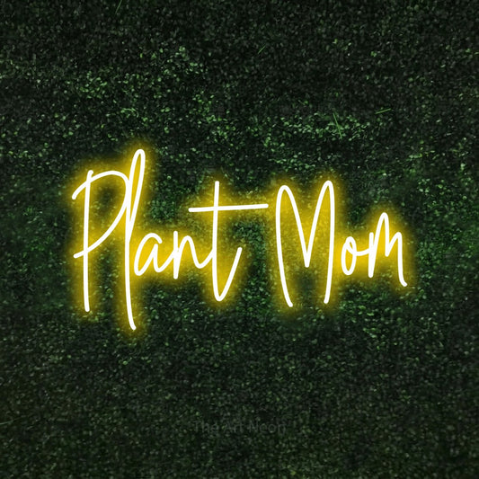 Yellow script-style LED neon sign reading "Plant Mom" against a textured green moss wall for living room décor