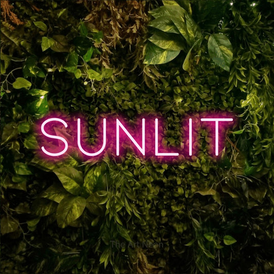 Hot pink LED neon sign reading "Sunlit" against a textured moss and foliage wall for living room décor