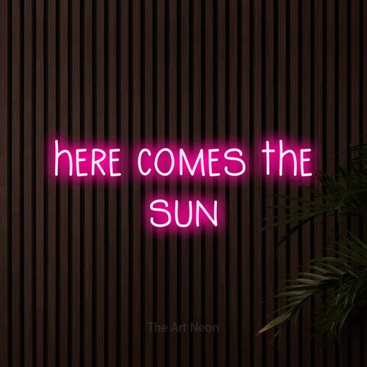 Hot pink LED neon sign reading "Here Comes the Sun" against dark wooden slats for living room décor
