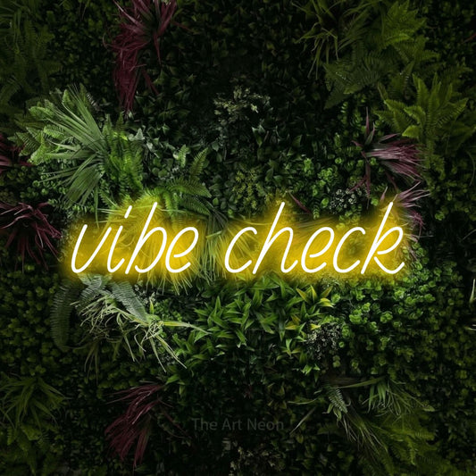Yellow LED neon sign reading "Vibe Check" against a lush garden wall with pink flowers for living room décor