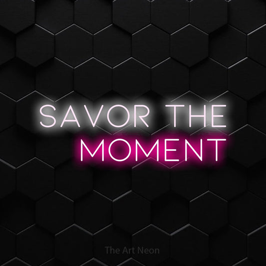 Hot pink and cool white LED neon sign reading "Savor the Moment" against a black hexagonal wall for living room décor