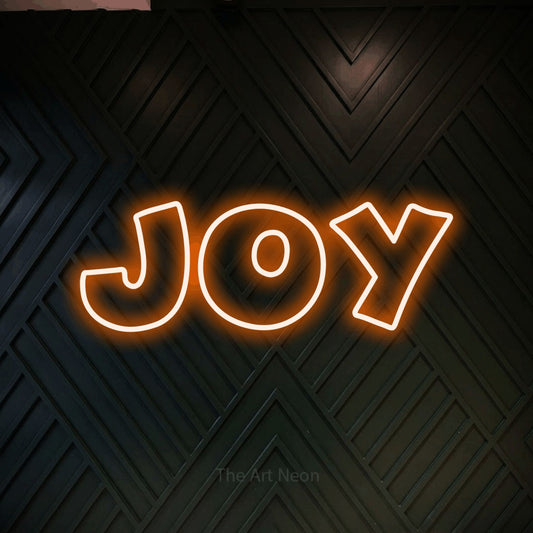 Orange outline-style LED neon sign reading "Joy" against a dark geometric wood wall for living room décor