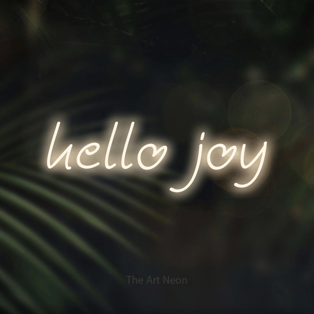 Warm white LED neon sign reading "Hello Joy" against dark blurred palm leaves for living room décor