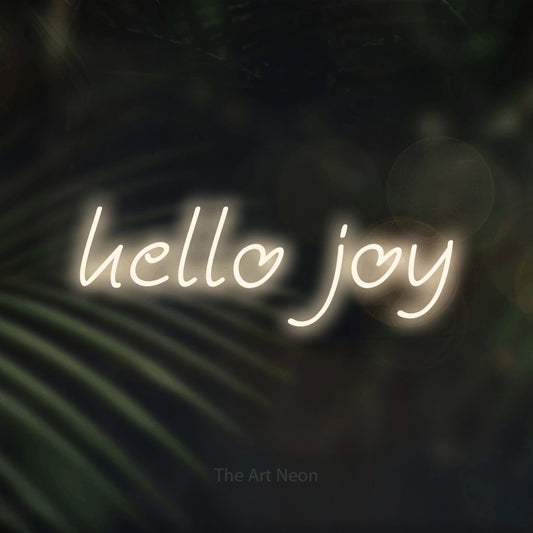 Warm white LED neon sign reading "Hello Joy" against dark blurred palm leaves for living room décor