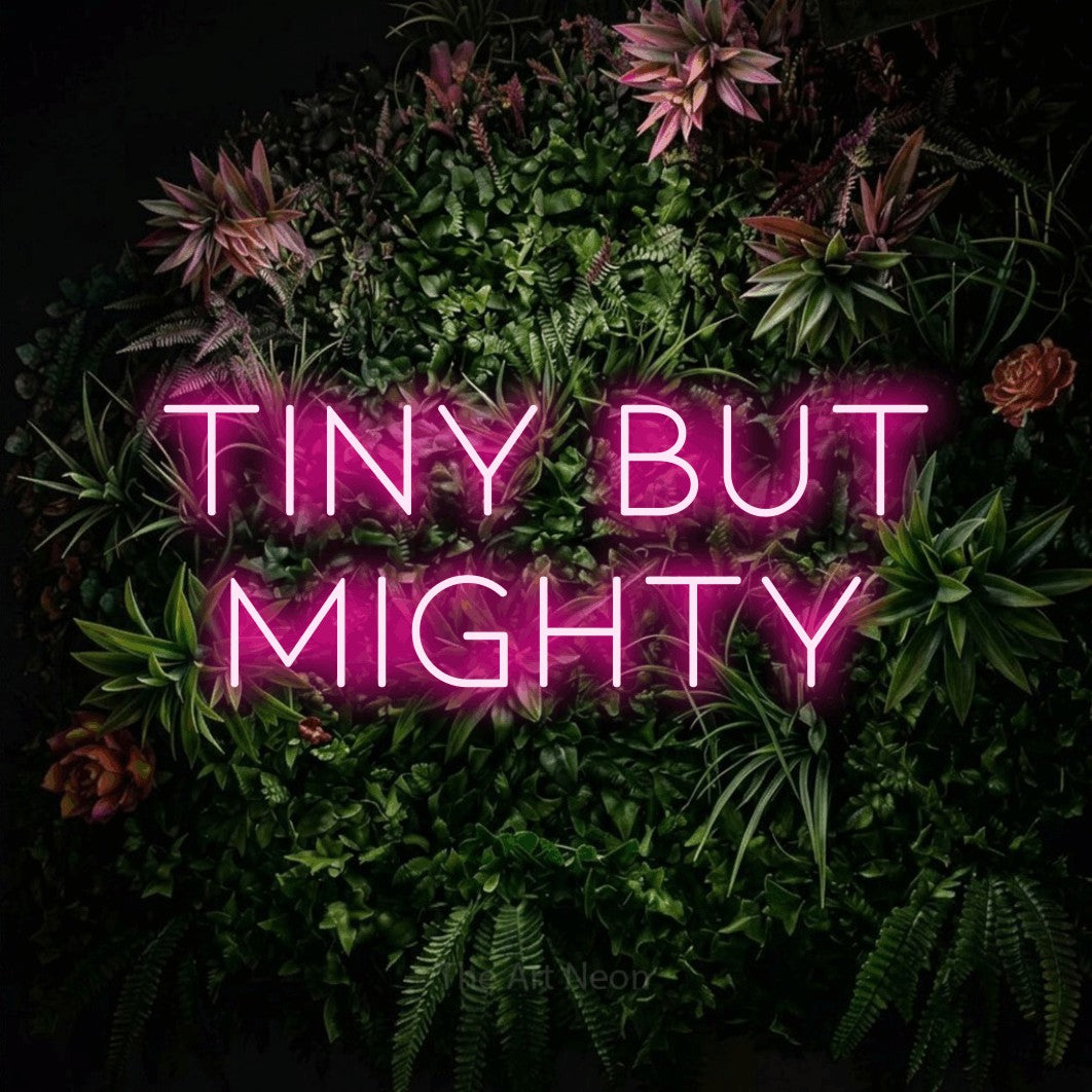 Enseigne néon à DEL à lumière rose vif, affichant « Tiny but Mighty » sur un mur de jardin fleuri, pour décorer une chambre de bébé