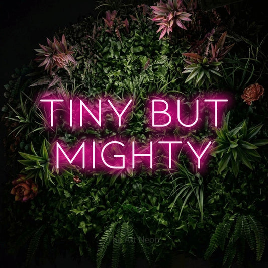 Enseigne néon à DEL à lumière rose vif, affichant « Tiny but Mighty » sur un mur de jardin fleuri, pour décorer une chambre de bébé