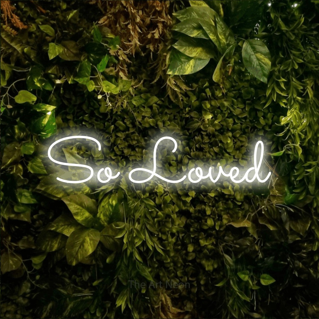 Enseigne néon à DEL à lumière blanche froide, affichant « So Loved » sur un mur texturé de mousse et de feuillage, pour décorer une chambre de bébé