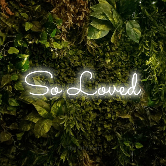 Enseigne néon à DEL à lumière blanche froide, affichant « So Loved » sur un mur texturé de mousse et de feuillage, pour décorer une chambre de bébé