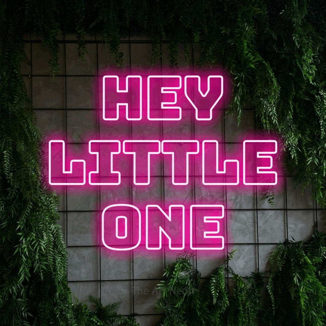 Enseigne néon à DEL à lumière rose vif, de style contour, affichant « Hey Little One » sur un mur quadrillé vert avec du feuillage, pour décorer une chambre de bébé