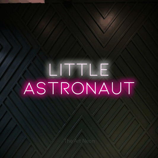 Hot pink and cool white LED neon sign reading "Little Astronaut" against a dark geometric wood wall for nursery décor