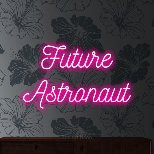 Hot pink script-style LED neon sign reading "Future Astronaut" against grey floral wallpaper for nursery décor