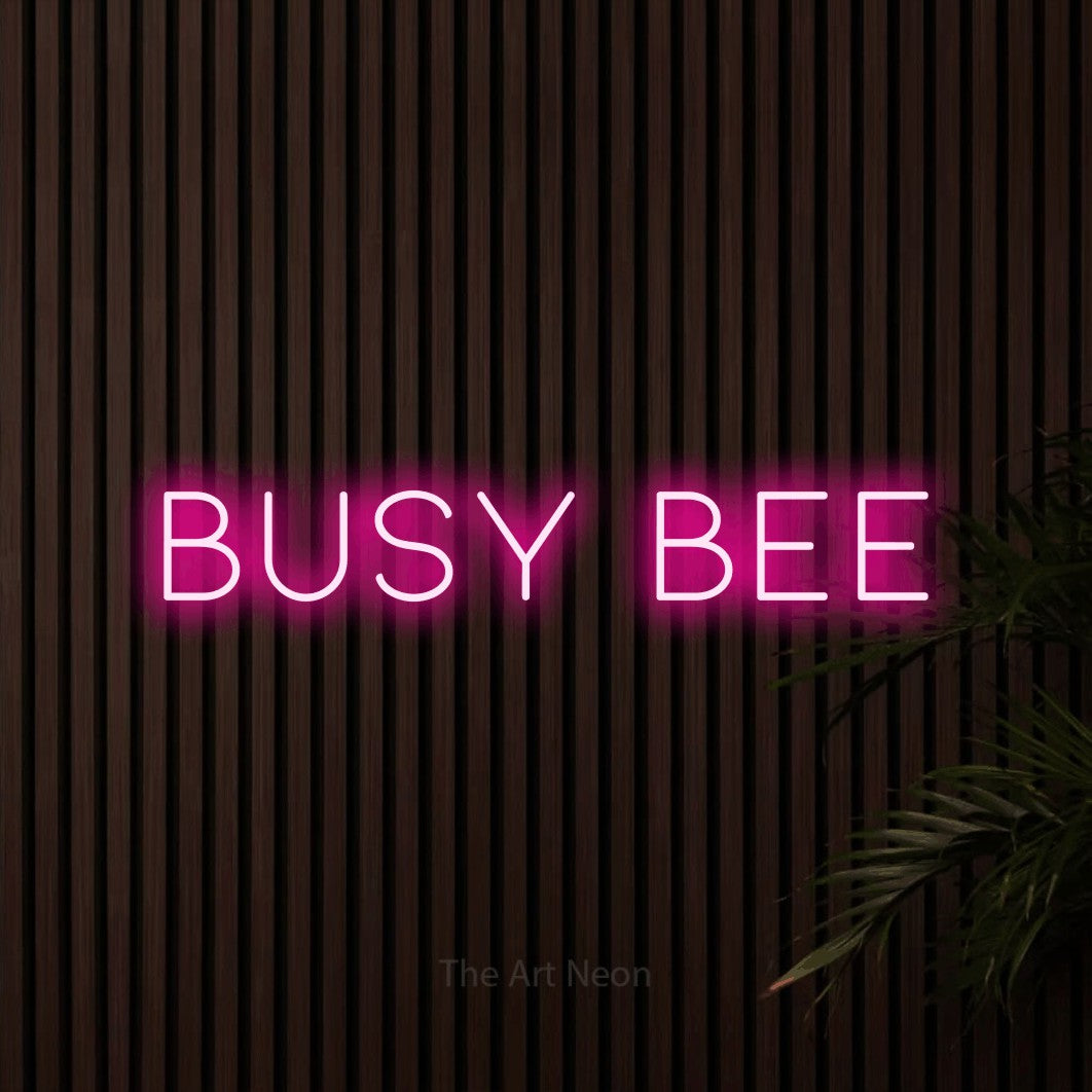 Hot pink LED neon sign reading "Busy Bee" against dark wooden slats for nursery décor