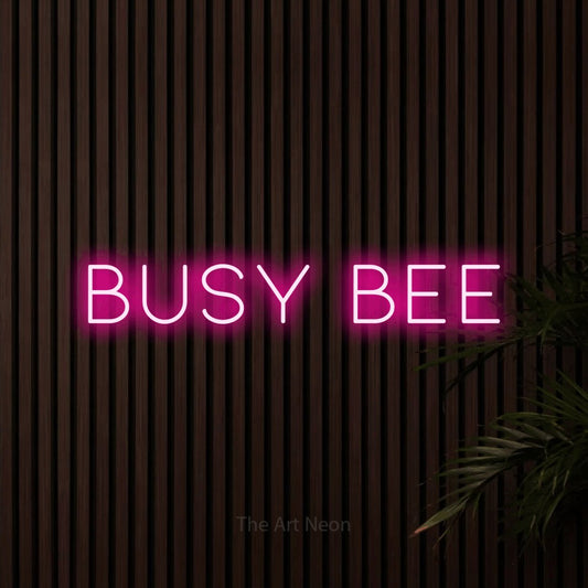 Hot pink LED neon sign reading "Busy Bee" against dark wooden slats for nursery décor