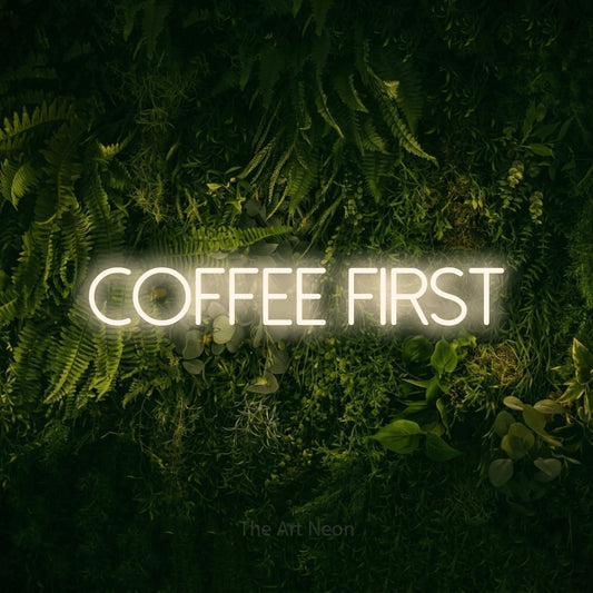 Warm white LED neon sign reading "Coffee First" against a moss-covered green wall for kitchen décor
