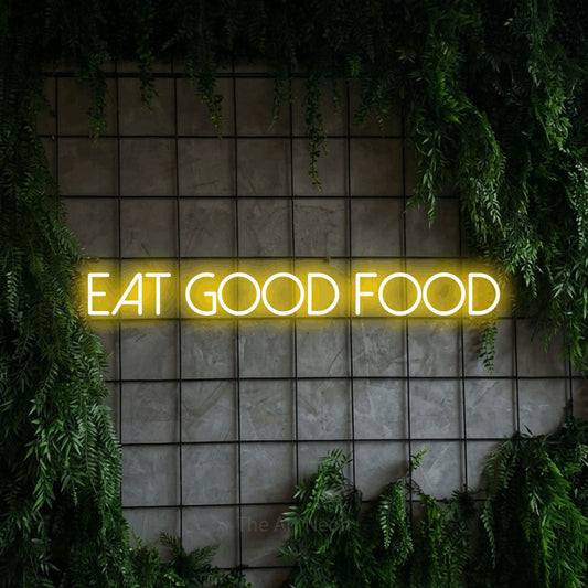 Yellow LED neon sign reading "Eat Good Food" against a green grid wall with foliage for kitchen décor