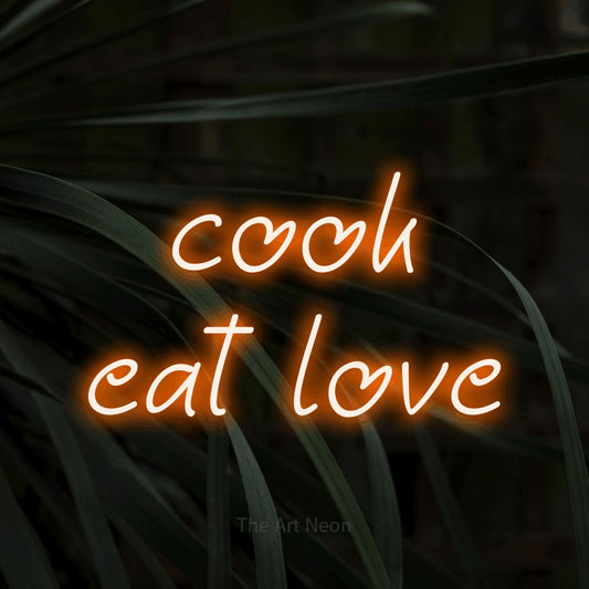 Orange LED neon sign reading "Cook Eat Love" against dark tropical leaves for kitchen décor
