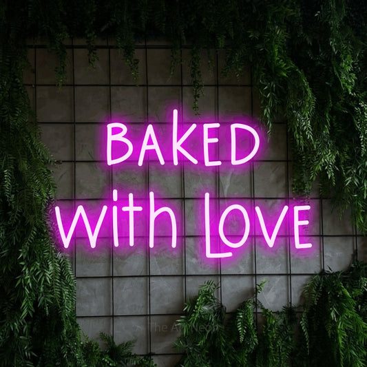 Pink LED neon sign reading "Baked with Love" against a green grid wall with foliage for kitchen décor