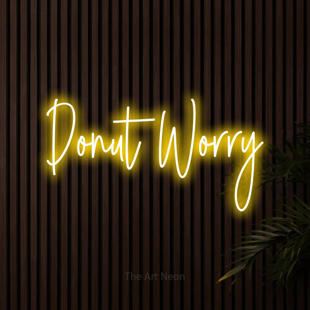Yellow script-style LED neon sign reading "Donut Worry" against dark wooden slats for kitchen décor