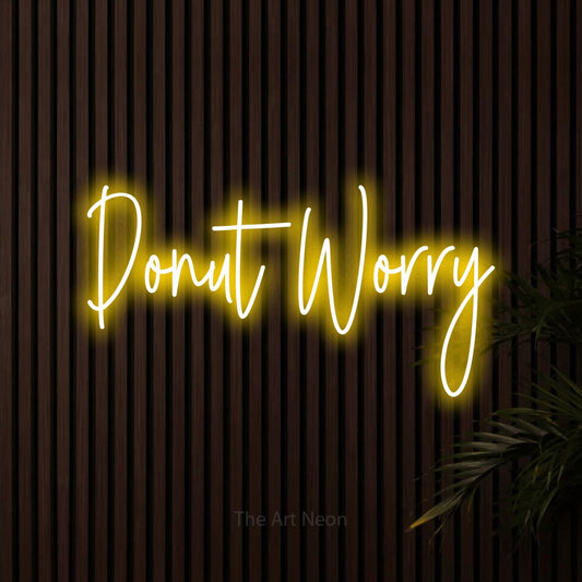 Yellow script-style LED neon sign reading "Donut Worry" against dark wooden slats for kitchen décor