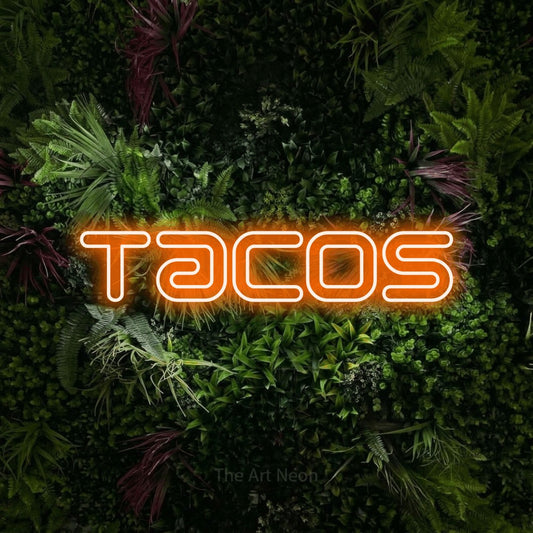 Orange outline-style LED neon sign reading "Tacos" against a lush garden wall with pink flowers for kitchen décor