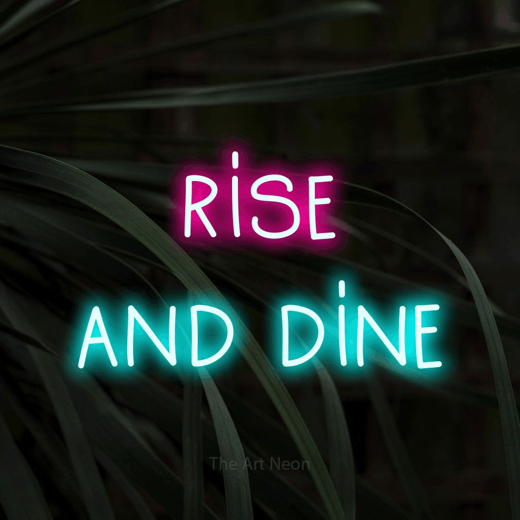 Ice blue and hot pink LED neon sign reading "Rise and Dine" against dark tropical leaves for kitchen décor