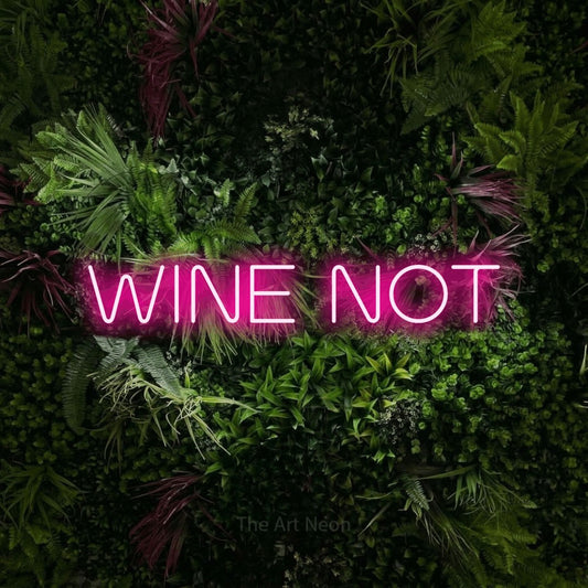 Hot pink LED neon sign reading "Wine Not" against a lush garden wall with pink flowers for kitchen décor