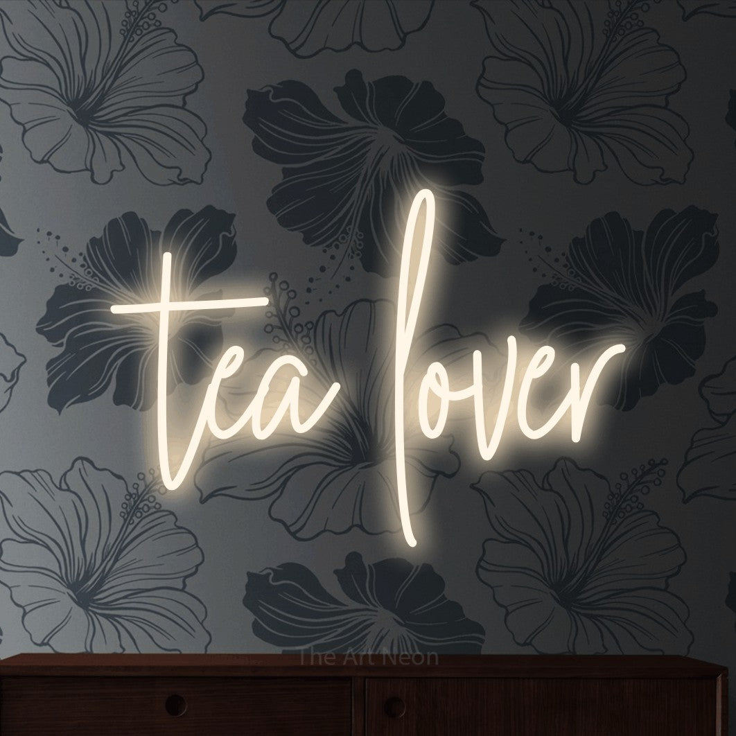 Warm white script-style LED neon sign reading "Tea Lover" against grey floral wallpaper for kitchen décor