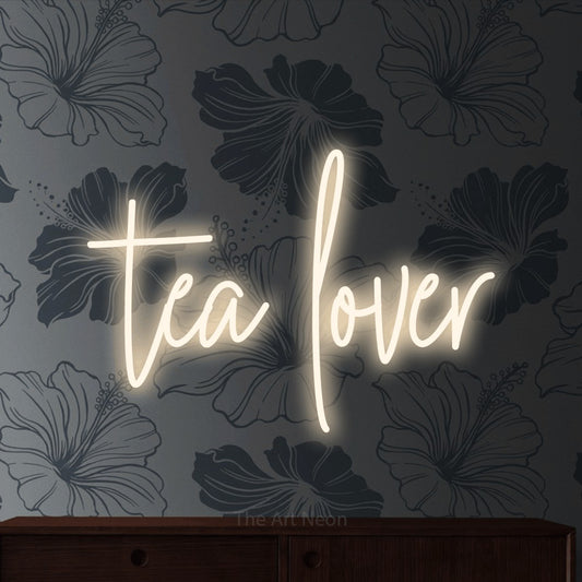 Warm white script-style LED neon sign reading "Tea Lover" against grey floral wallpaper for kitchen décor