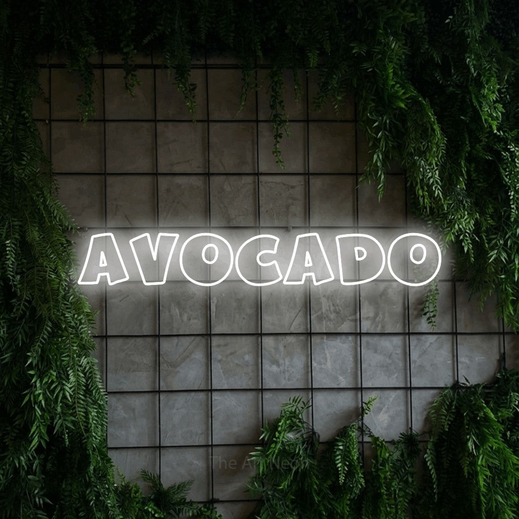 Cool white outline-style LED neon sign reading "Avocado" against a green grid wall with foliage for kitchen décor