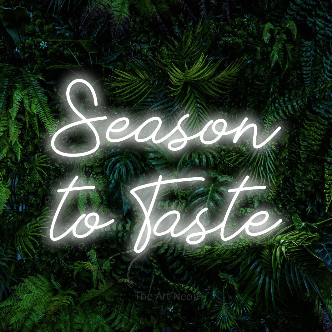 Cool white script-style LED neon sign reading "Season to Taste" against a dense tropical foliage wall for kitchen décor