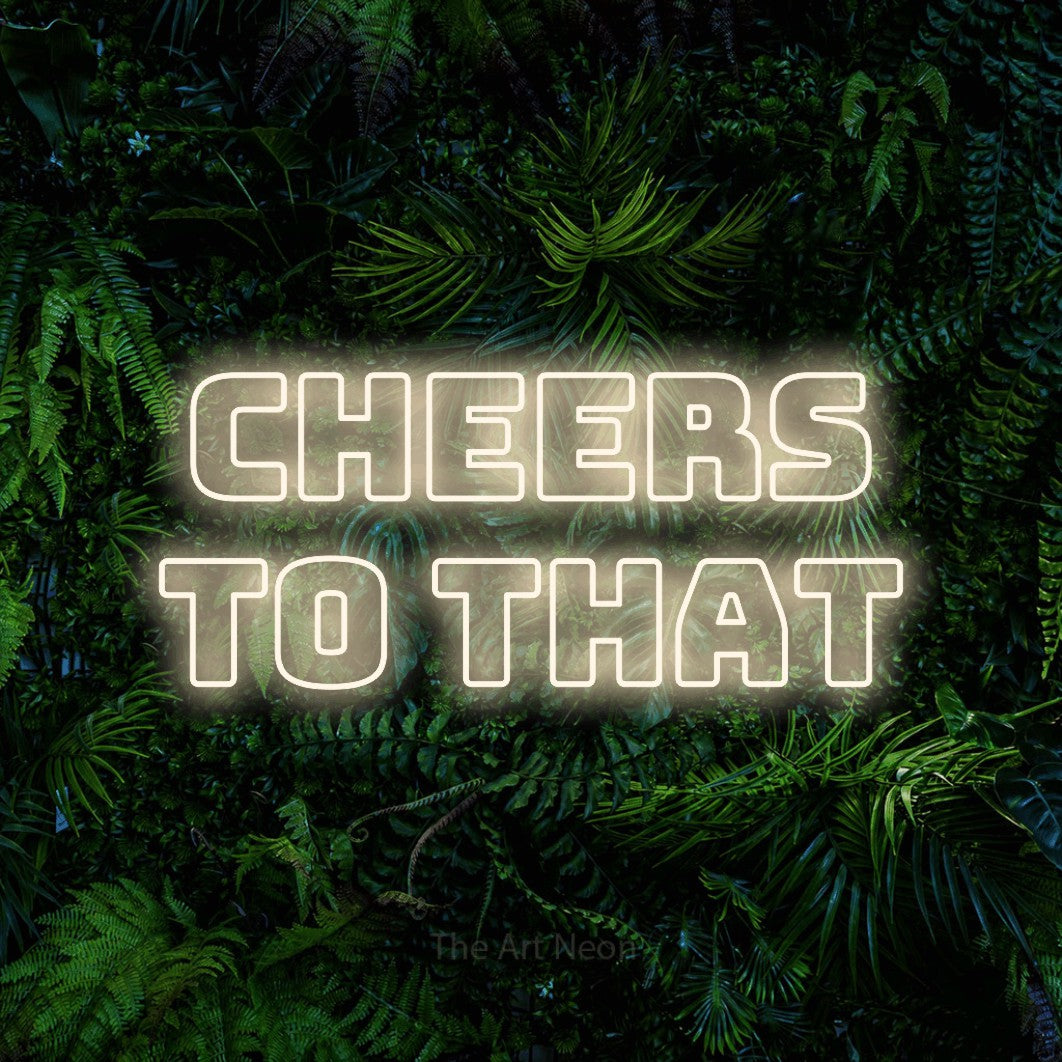 Warm white outline-style LED neon sign reading "Cheers to That" against a dense tropical foliage wall for bar décor