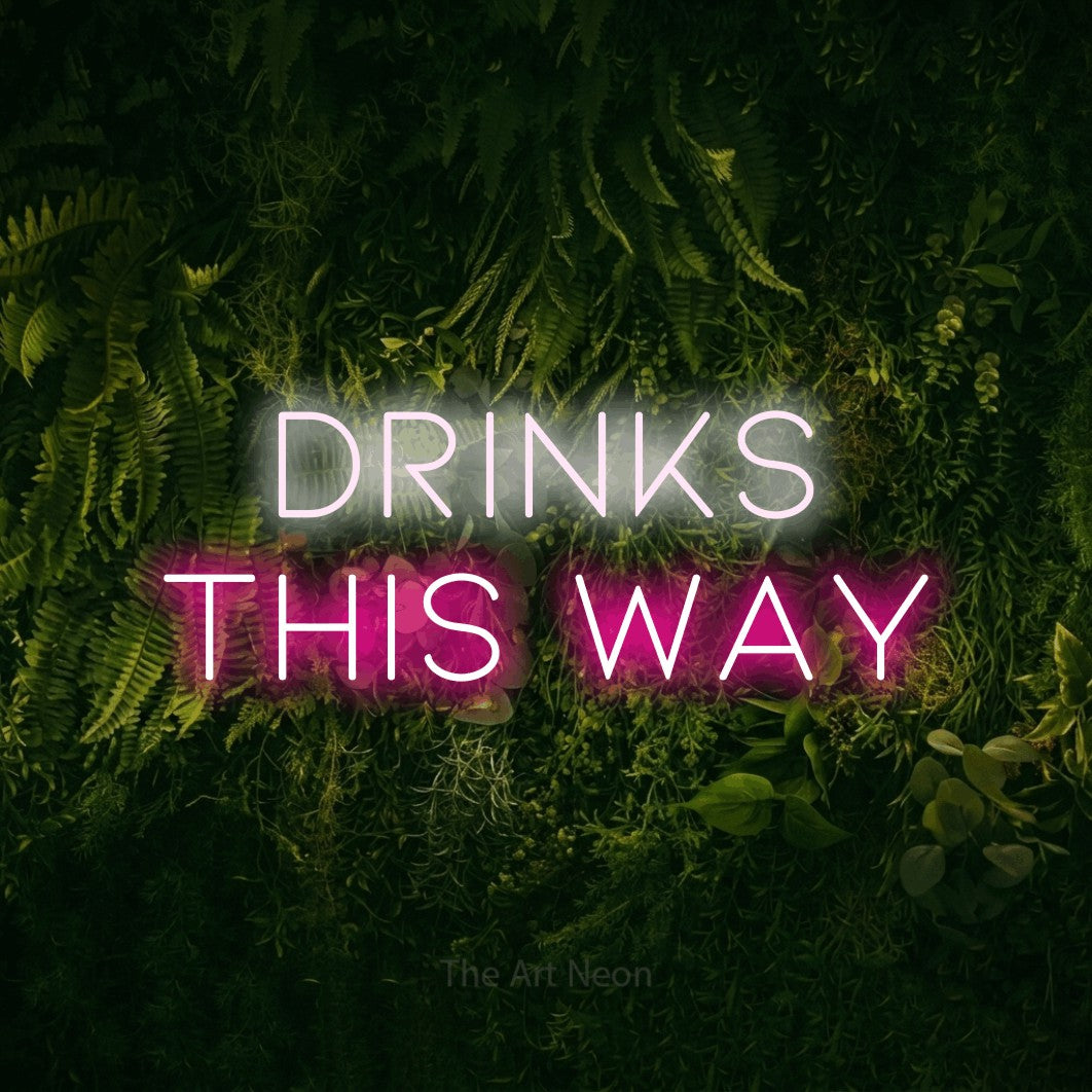 Hot pink and cool white LED neon sign reading "Drinks This Way" against a moss-covered green wall for bar décor