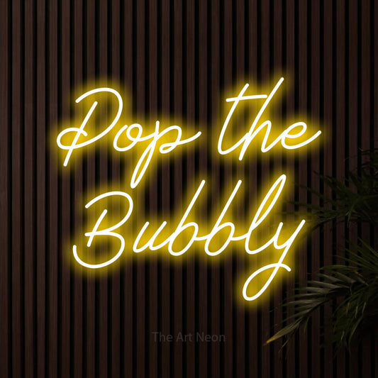 Yellow script-style LED neon sign reading "Pop the Bubbly" against dark wooden slats for bar décor