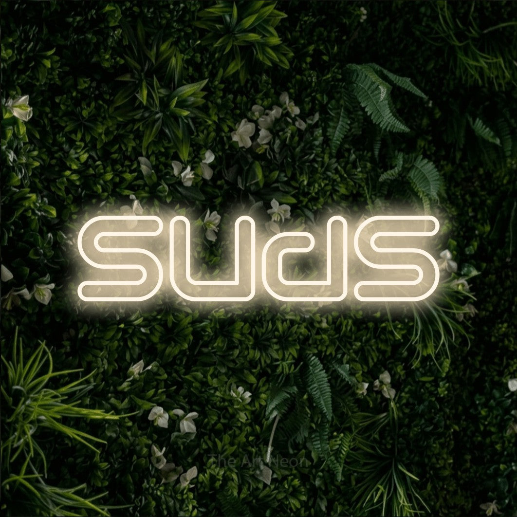 Warm white outline-style LED neon sign reading "Suds" against a leafy green wall for bar décor