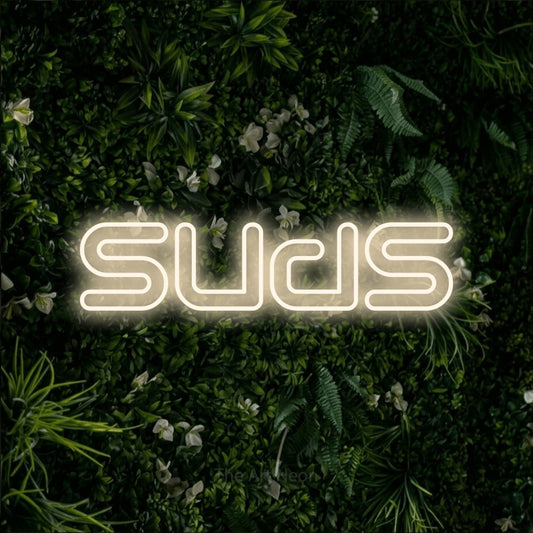 Warm white outline-style LED neon sign reading "Suds" against a leafy green wall for bar décor