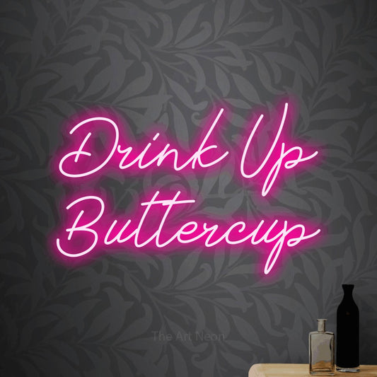 Hot pink script-style LED neon sign reading "Drink Up Buttercup" against light grey floral wallpaper for bar décor