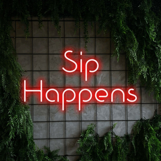 Red LED neon sign reading "Sip Happens" against a green grid wall with foliage for bar décor