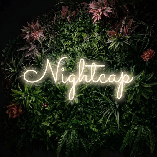Warm white LED neon sign reading "Nightcap" against a flowering garden wall for bar décor