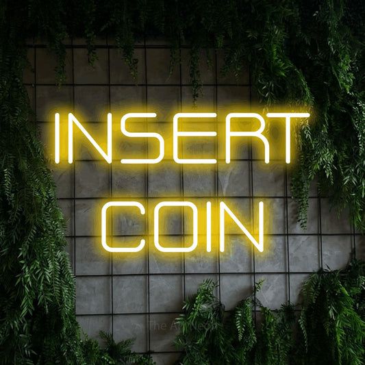 Yellow LED neon sign reading "Insert Coin" against a green grid wall with foliage for gaming room décor