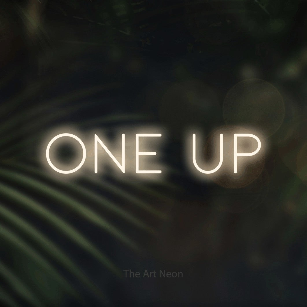 Enseigne néon à DEL à lumière blanche chaude, de style contour, affichant « One Up » sur des feuilles de palmier foncées et floues, pour décorer une salle de jeu