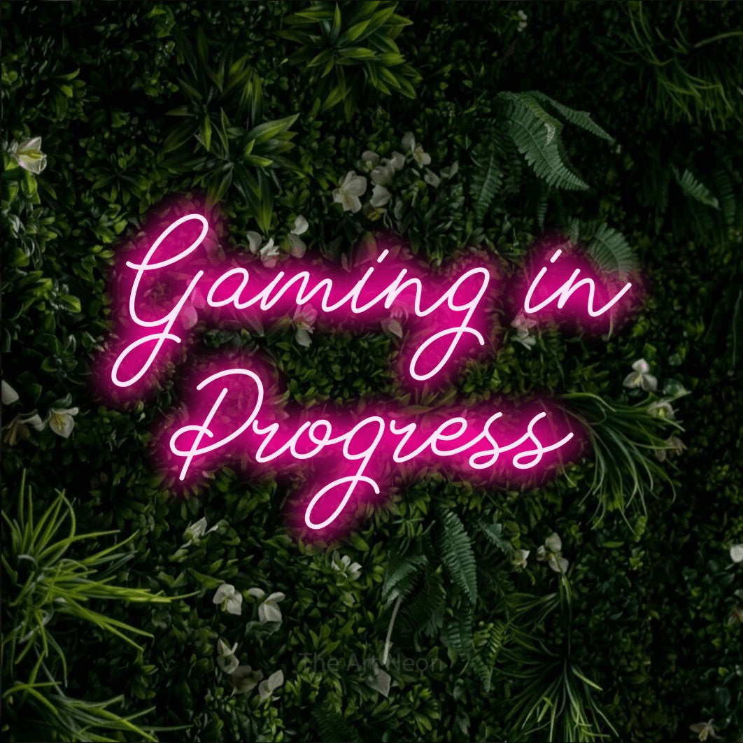 Enseigne néon à DEL à lumière rose vif, de style manuscrit, affichant « Gaming in Progress » sur un mur de feuillage vert, pour décorer une salle de jeu